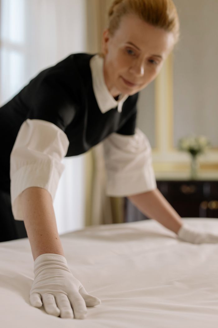 A housekeeper carefully and elegantly arranges the bed sheets in an upscale hotel room, highlighting hospitality know-how.